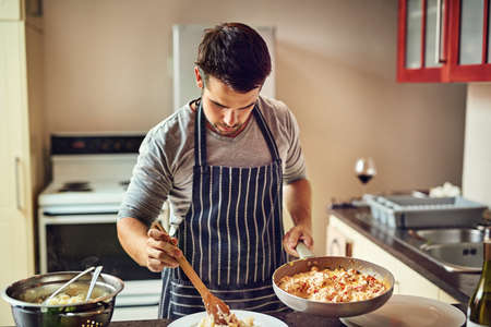 I enjoy the whole process of cooking beginning to end. Shot of a young man preparing food in the kitchen at home.の写真素材