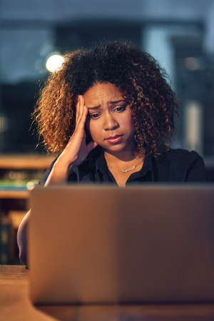 Its just one thing after another. Shot of a young businesswoman experiencing stress during a late night at work.の写真素材