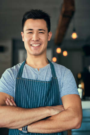 Hes got confidence in his coffee shop. Cropped portrait of a young man standing with his arms folded in his coffee shop.の写真素材
