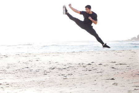 Kicking it into high gear. Full length shot of a handsome young male athlete working out on the beach.の写真素材