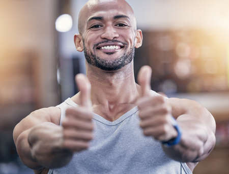 Here to support your life-changing fitness journey. Portrait of a muscular young man showing thumbs up in a gym.の写真素材