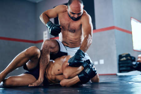 Its all about tactics. Shot of a male fighter about to punch another male fighter while in combat on the floor at the gym.の写真素材