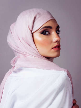 Her look catches everyones attention. Studio portrait of a cheerful young woman wearing a colorful head scarf while posing against a grey background.の写真素材