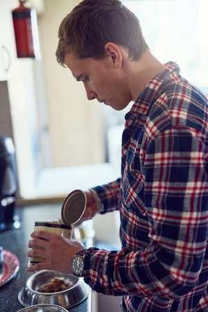 Chow time. Shot of a young man filling a bowl with pet food at home.