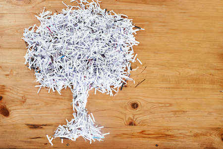 Save the environment. Recycle. Studio shot of shredded paper arranged in the shape of a tree on a wooden table.の写真素材
