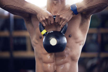 He hustled, he got that muscle. Shot of an unrecognisable man working out with a kettle bell at the gym.の写真素材