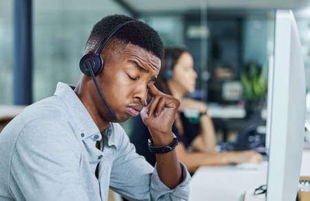 So much to get done today. Shot of a young call centre agent looking tired in an office.の写真素材
