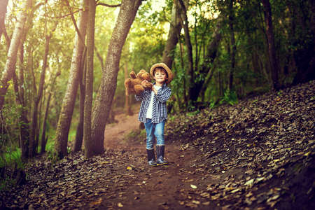Teddy and I are quite excited about this adventure. Shot of a little boy sitting in the forest with his teddy bear.の写真素材
