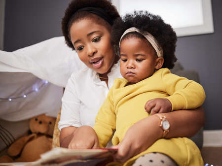 What are we reading today. Shot of a young mother and daughter reading a book at home.の写真素材