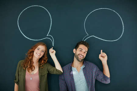 Making themselves heard. Portrait of a young couple standing in front of a blackboard with speech...