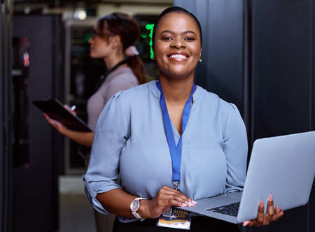Ill have your servers performing optimally. Cropped portrait of an attractive young female programmer working in a server room with her colleague in the background.の写真素材