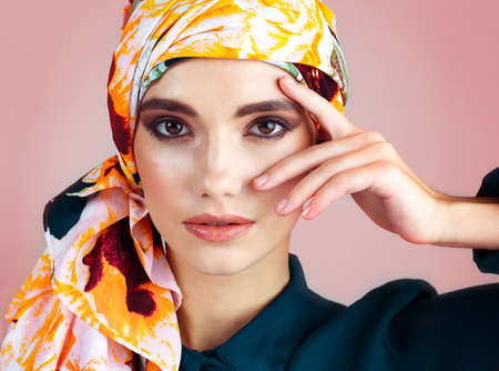 She looks right into your soul. Studio portrait of a confident young woman wearing a colorful head scarf while posing against a pink background.の写真素材