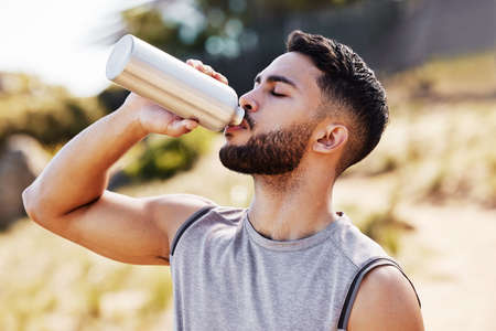 Staying hydrated is how I can keep going. Shot of a handsome young man standing alone outside and...