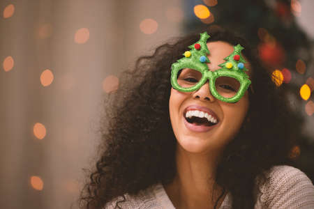 Its not just the Christmas tree that sparkles. Portrait of a young woman fun glasses during Christmas at home.の写真素材
