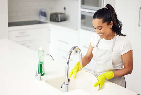 Dishes are a never-ending story, best you start enjoying it. Shot of a young woman washing dishes in...