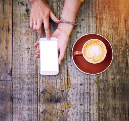 Grab some coffee and join the conversation. High angle shot of a woman using her cellphone and having a cup of coffee.の写真素材