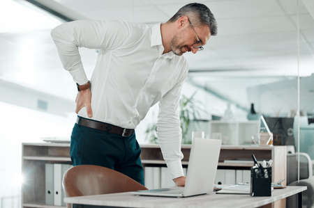 Ooo, my back is killing me. Shot of a mature businessman standing alone in his office and suffering...