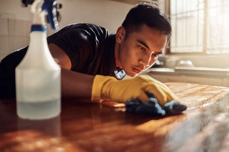 As squeaky clean as a kitchen should be. Shot of a young man disinfecting a kitchen counter at home.の写真素材