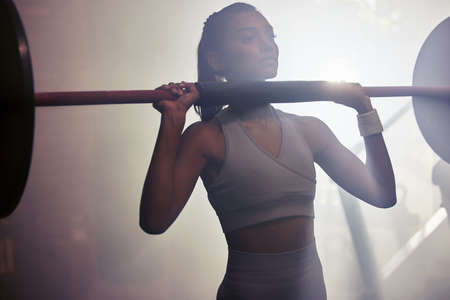 Witness her fitness. Shot of a sporty young woman getting ready to do a barbell overhead press in a...