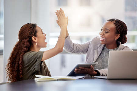 I couldnt have done it without you. Shot of two young female colleagues giving each other a high...