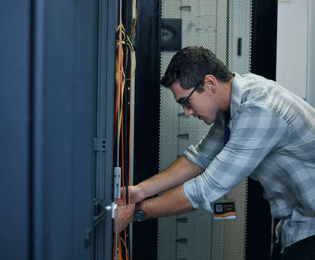 Hes the technician you need. Cropped shot of a handsome young male programmer working in a server room.の写真素材