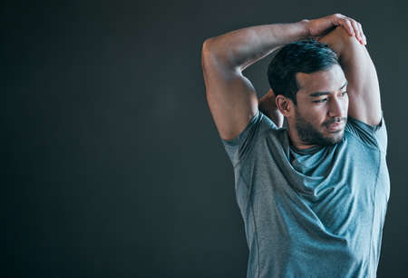 Getting in a good pre-workout warmup. Cropped shot of a handsome young male athlete warming up against a grey background.の写真素材
