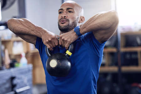 A strong mind makes a strong body. Shot of a young man working out with a kettle bell at the gym.