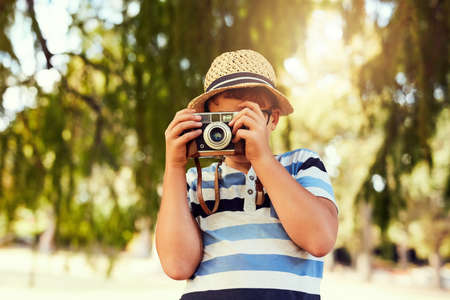 Seeing the world in a new light. Shot of a little boy taking a photo with a vintage camera at the park.の写真素材