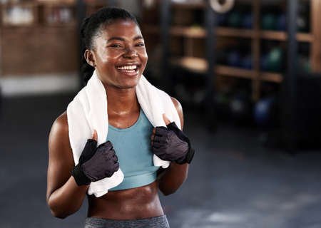 Fit and happy. Shot of a sporty young woman posing with a towel around her neck at gym.の写真素材