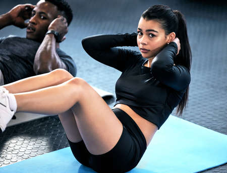 We dont do lunch dates, we do crunch dates. Shot of a young man and woman doing sit ups in a gym.