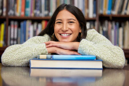 Explore and achieve. Shot of a young woman resting on a pile of books in a college library.の写真素材