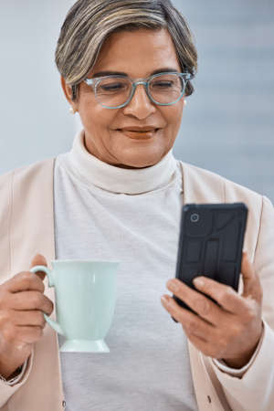 Theres always time for tea and business. Shot of a mature businesswoman drinking coffee while using...