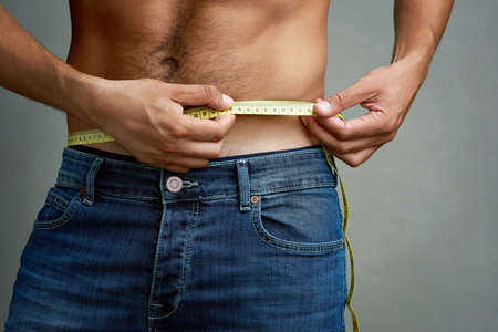 Youll only get the body you work for. Studio shot of an unidentifiable man measuring his torso against a grey background.の写真素材