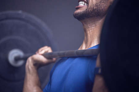Hard work, hard muscles. Shot of an unrecognisable man working out with a barbell at the gym.の写真素材