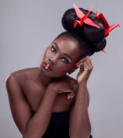 Dazzle the world with your uniqueness. Studio portrait of a beautiful young woman wearing Asian inspired makeup and posing with origami against a grey background.の写真素材