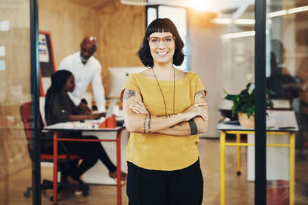 Its a good feeling to succeed. Shot of a creative businesswoman standing in her office with colleagues blurred in the background.の写真素材