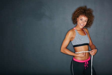Progress is impossible without change. Portrait of a sporty young woman measuring her waist against a grey background.の写真素材