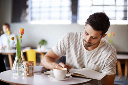 The write stuff. Shot of a handsome young man writing in a notebook while sitting at a restaurant...