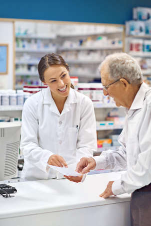 Filling prescriptions with a smile. Shot of a young pharmacist helping an elderly customer at the prescription counter.の写真素材