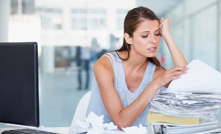 Buried under paperwork. Shot of a stressed out young businesswoman going through a stack of...