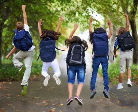 Spring break. Rear view of excited schoolchildren jumping in a row.の写真素材