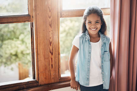 Happy kids make happy homes. Portrait of a happy young girl standing next to a window at home.の写真素材