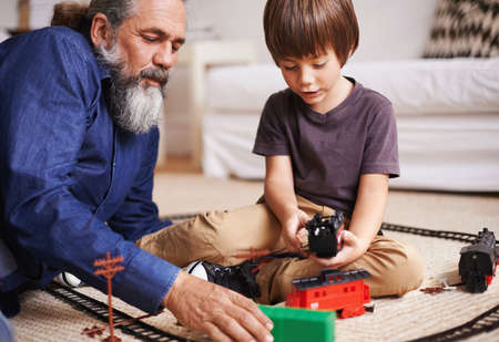 Ok grandpa, you be the conductor and Ill drive the train..... Cropped shot of a grandfather watching his grandson play with a toy train.の写真素材