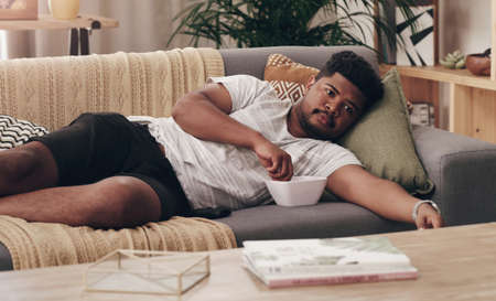 This is a much needed break. Shot of a young man lying on his couch at home.の写真素材