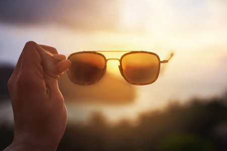 Life through rose-colored glasses. Cropped shot of an unidentifiable tourist holding up a pair of sunglasses over a tropical view.の写真素材