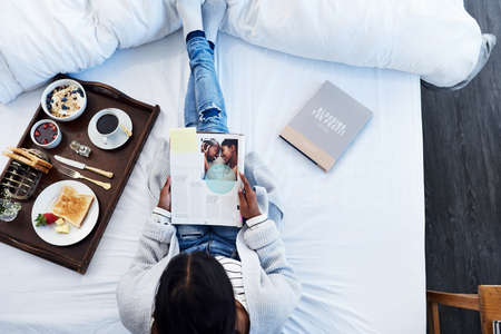 Breakfast in bed and some good books. High angle shot of an unrecognizable woman reading a magazine...