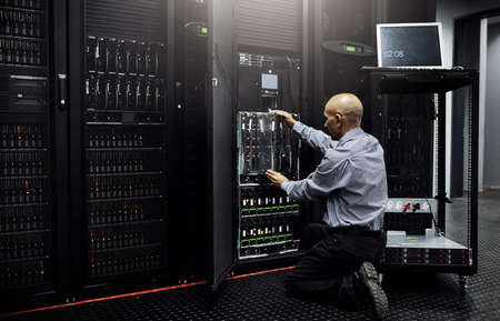 Hes well-versed in all things IT. Rearview shot of an IT technician repairing a computer in a data...