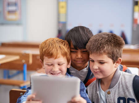 Checking out apps together. Cropped shot of elementary school children using a tablet in class.の写真素材