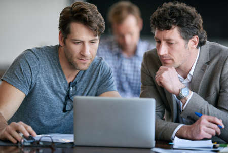 Interesting.... Cropped shot of two businessmen looking over some work with their colleague in the...