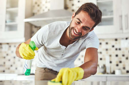 He loves it when things are clean. Cropped shot of a handsome young man cleaning his kitchen at home.の写真素材